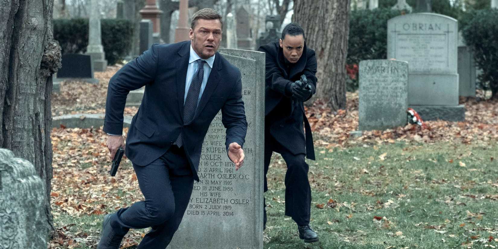 Maria Sten as Neagley and Alan Ritchson as Jack Reacher running through a cemetery with guns out in Reacher.