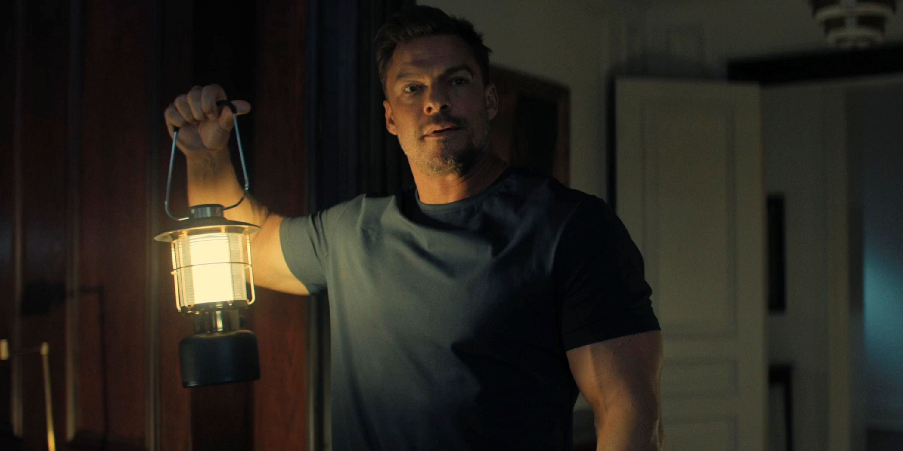 Alan Ritchson as Jack Reacher holding a lantern at night in Season 3 of Reacher