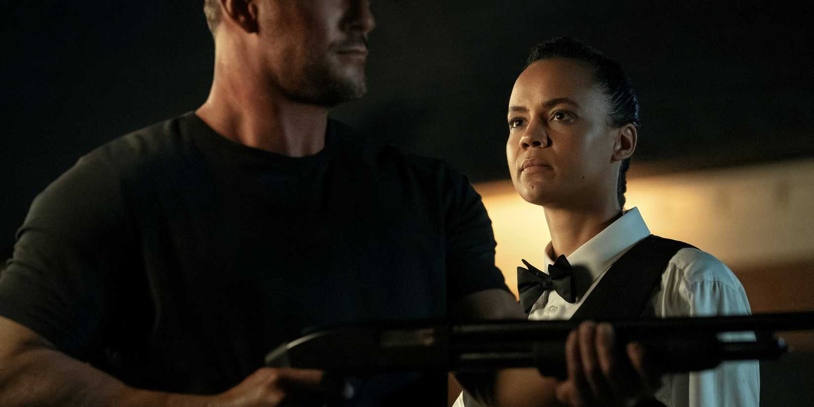 Maria Sten as Neagley dressed as a cater waiter behind Alan Ritchson as Jack Reacher holding a gun in 'Reacher.'
