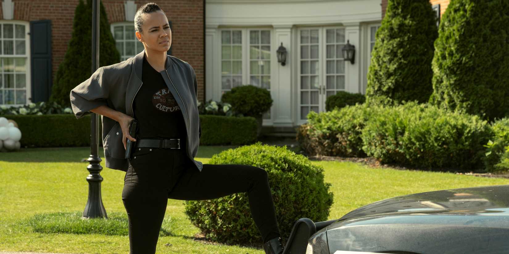 Maria Sten as Neagley with her left foot on the front bumper of a car in Season 3 of Reacher.