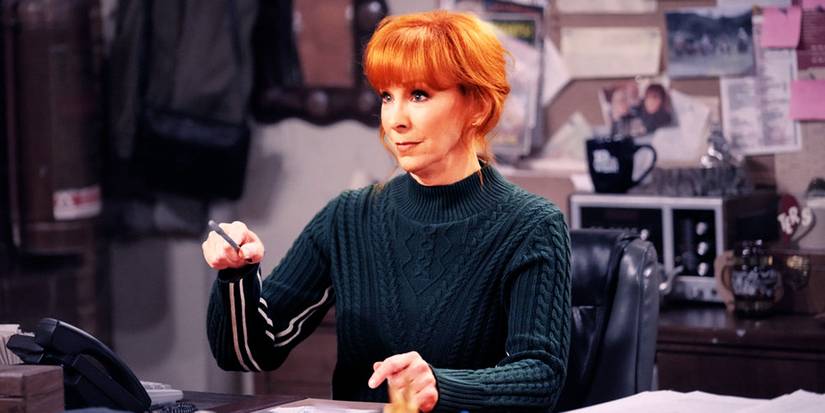 Reba McEntire wears a green sweater and points her pen off camera