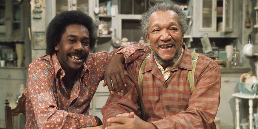 Redd Foxx and Demond Wilson sitting at a kitchen table and smiling in Sanford and Son.