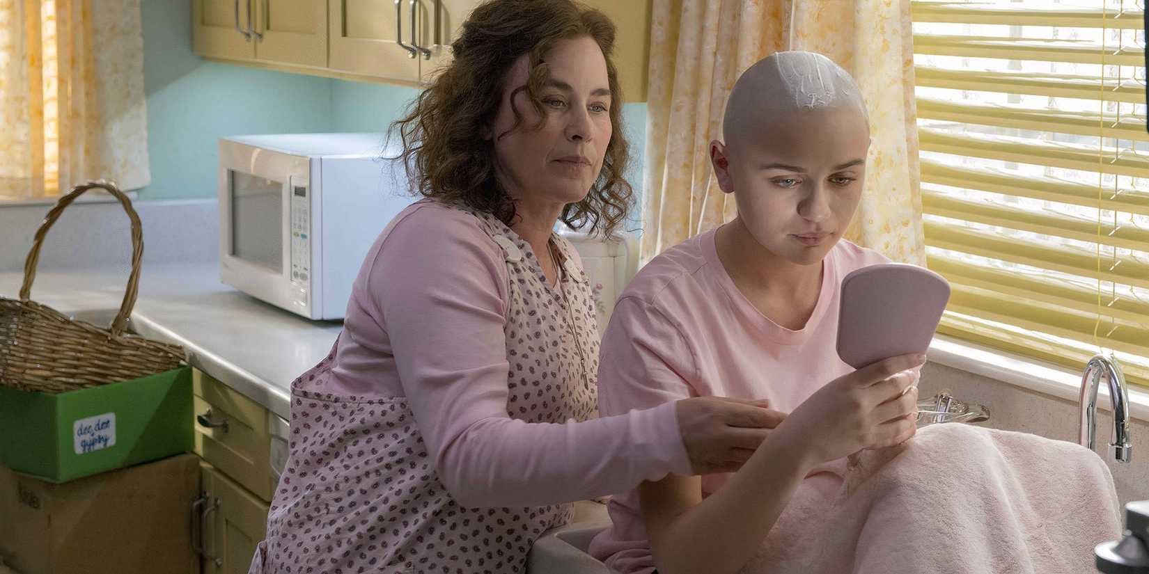 Gypsy holding a mirror and staring at her reflection, while Dee Dee stands slightly behind her in the series The Act.