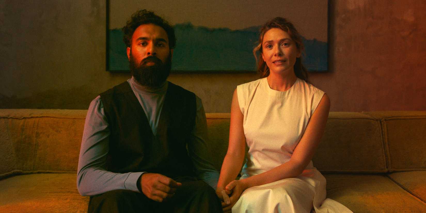 Elizbeth Olsen as Mia sitting on the couch next to Himesh Patel as Aaryan in The Assessment