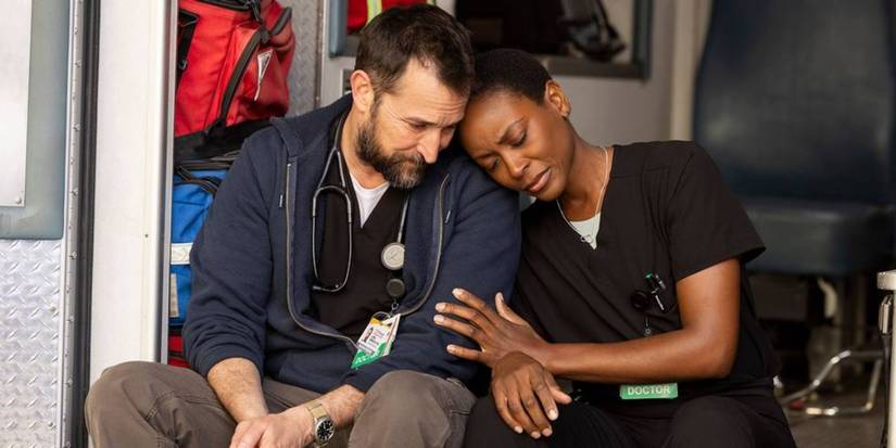 Heather (Tracy Ifeachor) leans against Robby (Noah Wyle), sitting on the back of an ambulance in The Pitt.