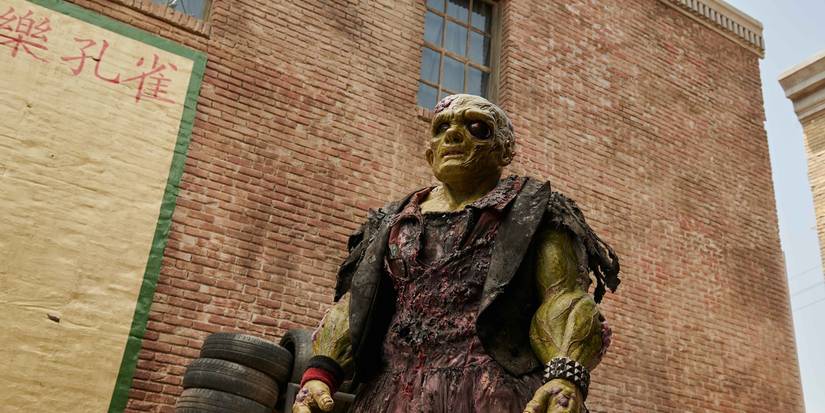 Peter Dinklage as The Toxic Avenger stands outside a building.