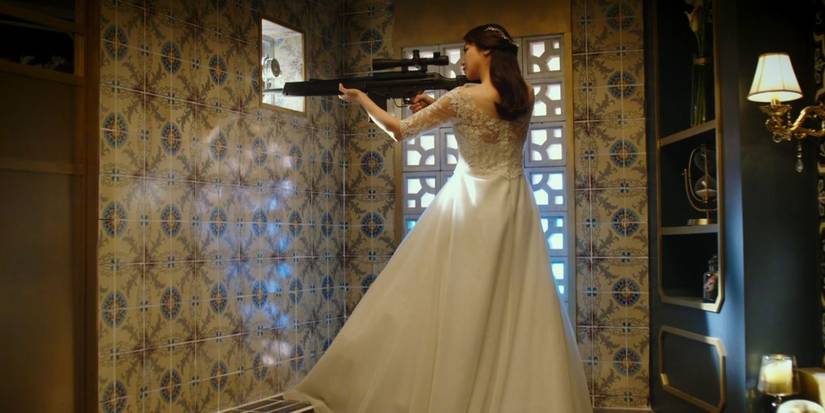 Sook-hee is in full bridal wear as she aims a sniper rifle through a bathroom's vent in The Villainess 