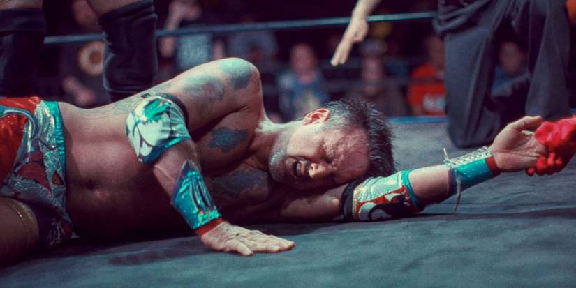 David Arquette lies on his side in a wrestling ring, looking pained and in wrestling garb