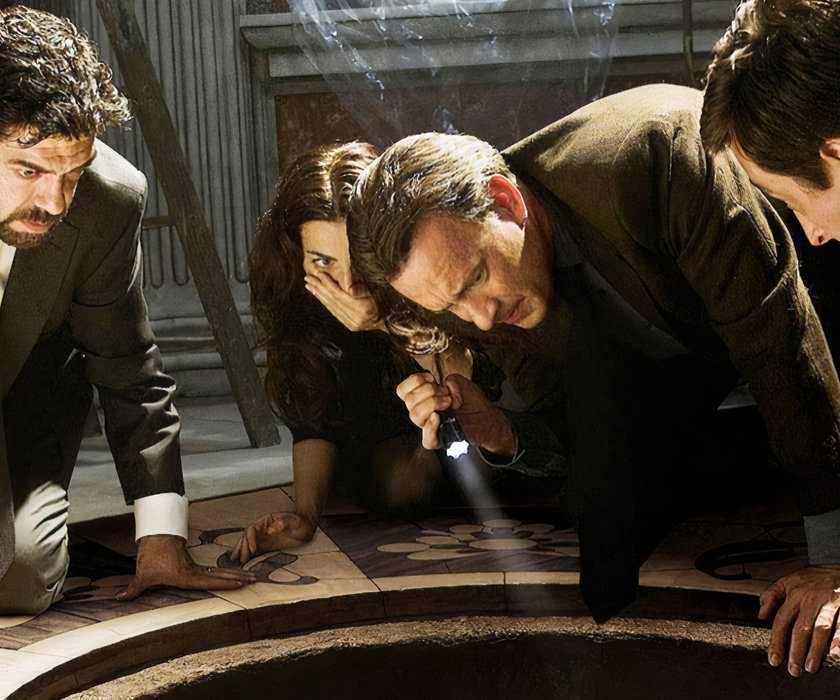 The cast crouch down on the floor looking at something below in a hole in Angels & Demons.