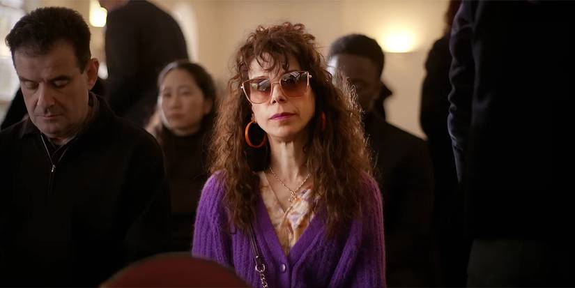 Laura sits in a purple outfit at a funeral in Bring Her Back.
