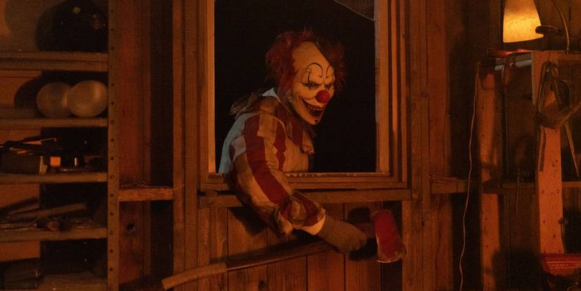 Clown in a Cornfield's Frendo holding an axe and leaning in through a window