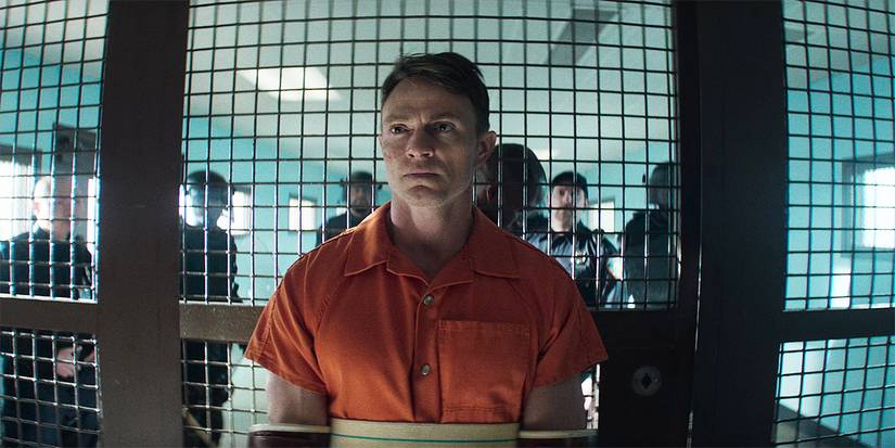 Wilson Bethel as Ben Poindexter/Bullseye in prison standing in front of the gate with guards behind him in Daredevil: Born Again