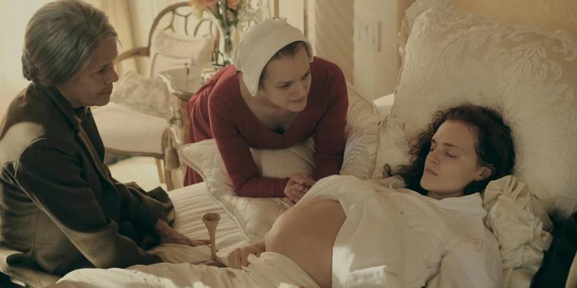 Janine (Madeline Brewer) lies in bed with her pregnant belly showing, with June standing (Elisabeth Moss) next to her in 'The Handmaid's Tale'