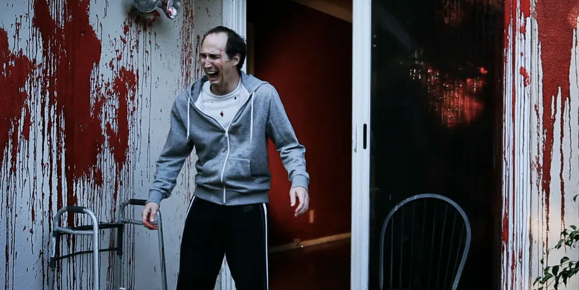 A man in running gear screams as the walls around him are surrounded with blood in The Human Race