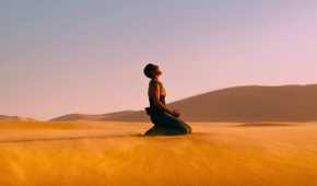 Furiosa, played by Charlize Theron, screams after falling to her knees on sand dunes in Mad Max: Fury Road.
