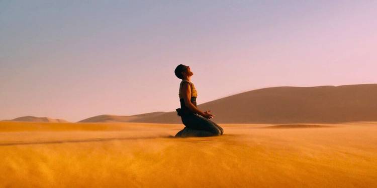 Furiosa, played by Charlize Theron, screams after falling to her knees on sand dunes in Mad Max: Fury Road.