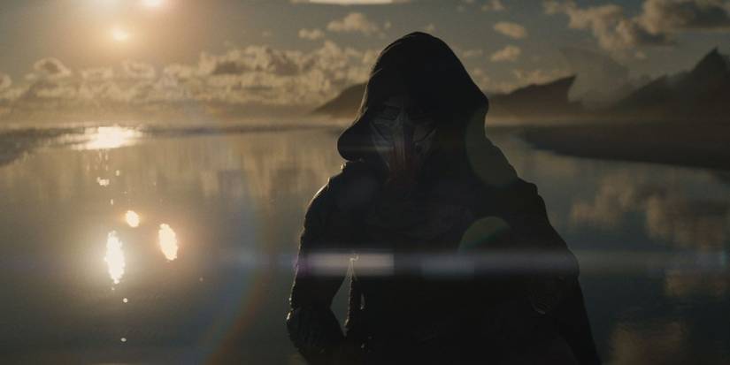A hooded figure stands in front of a sunset in Predator: Badlands