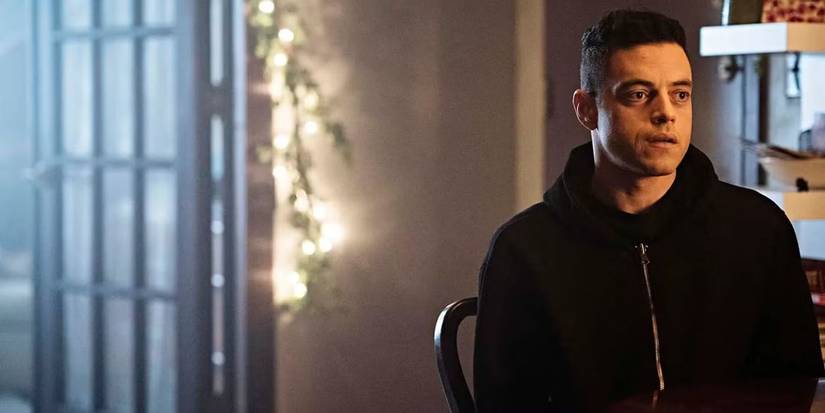 Rami Malek as Elliot in Mr. Robot sitting in a chair on the far right side of the screen with a window behind.