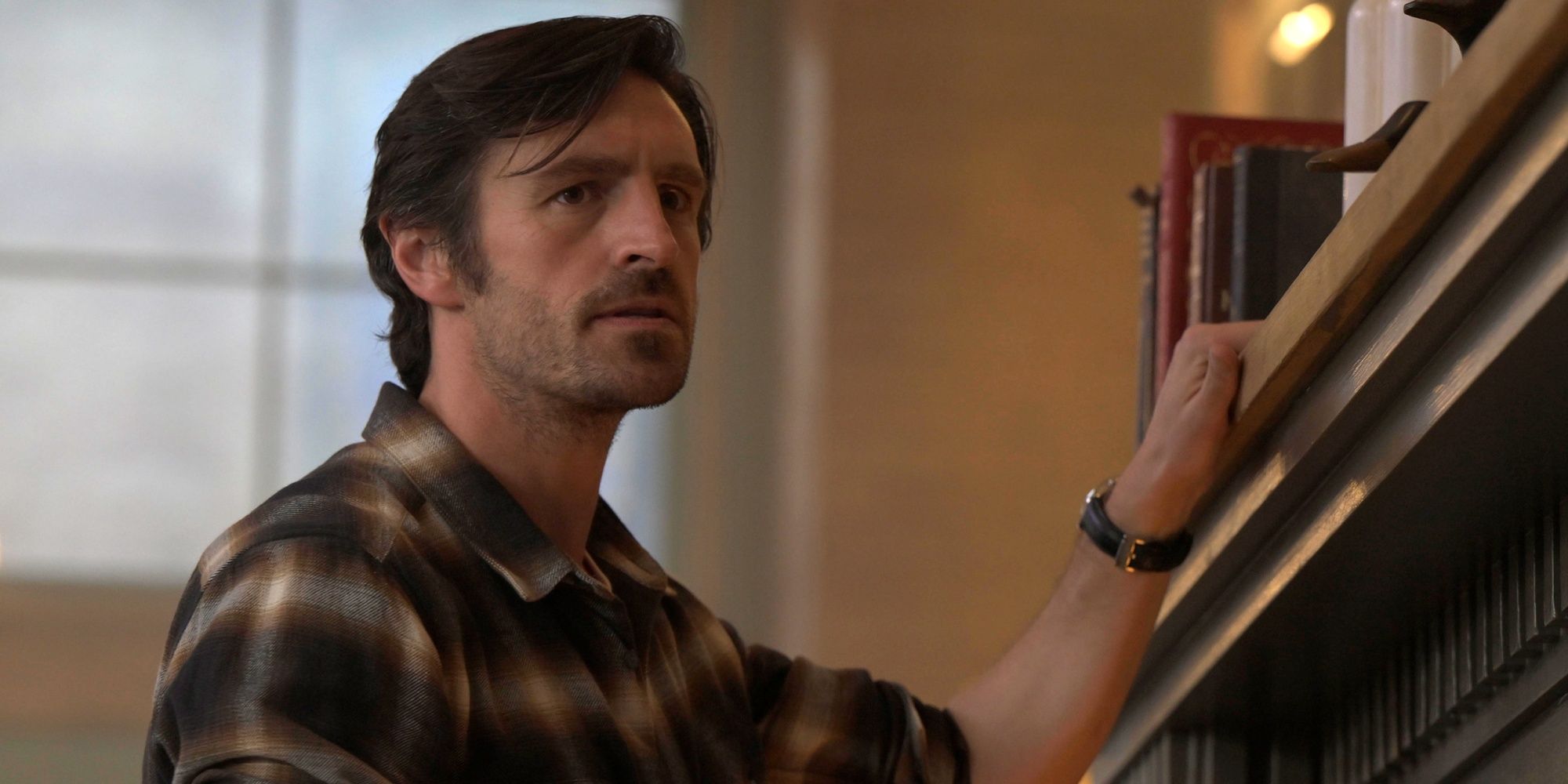 Eoin Macken as Davis Collins with his left hand up on the mantle in a plaid shirt in Ransom Canyon