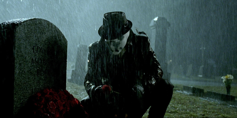 Jackie Earle Haley as Rorschach kneels in front of a grave on a rainy night in Watchmen.