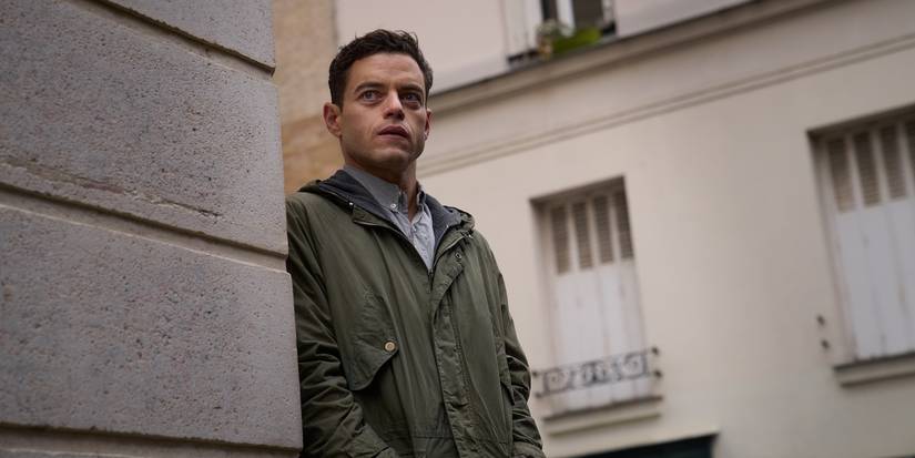 Rami Malek peeking around a building in The Amateur