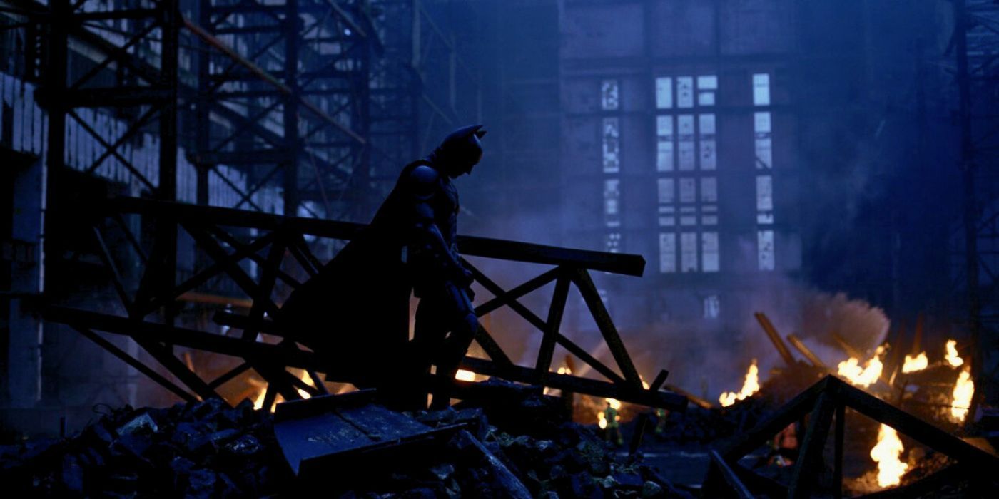 Batman stands in profile over the ruin of Joker's explosives in The Dark Knight.