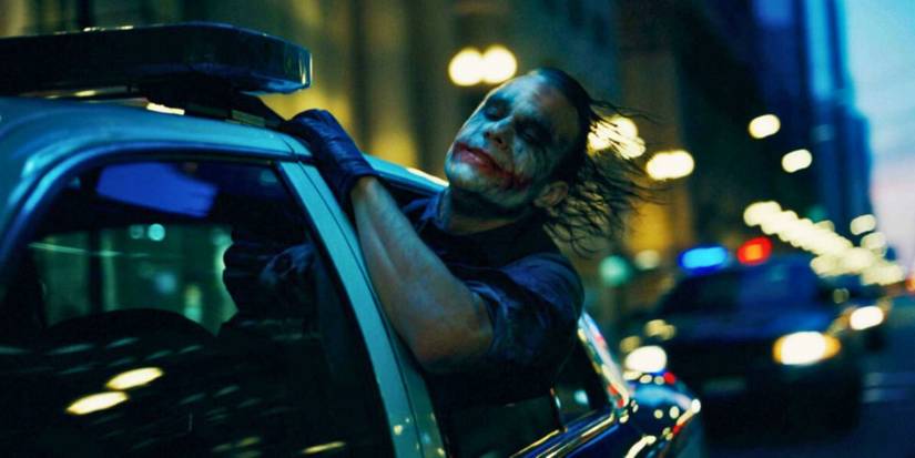 Heath Ledger as The Joker leans out of the window of a moving police car in The Dark Knight.
