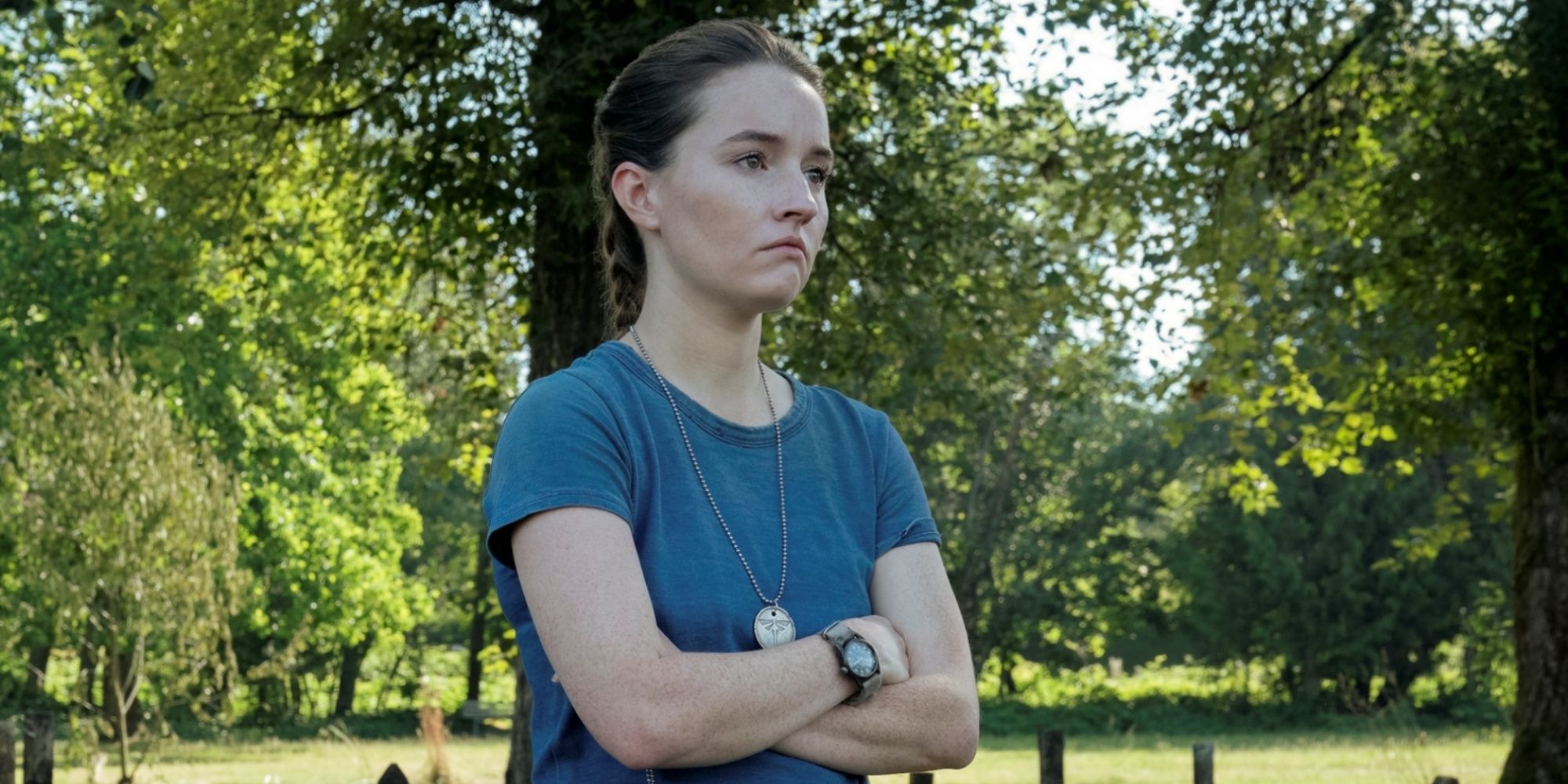 Kaitlyn Dever as Abby standing in a cemetery with her arms crossed in front of her in Season 2 of The Last of Us