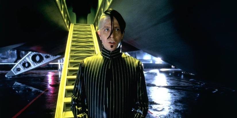 Zorg (Gary Oldman) at the bottom of a ramp, wearing a black pinstriped outfit with slick black hair and a soul patch in The Fifth Element.