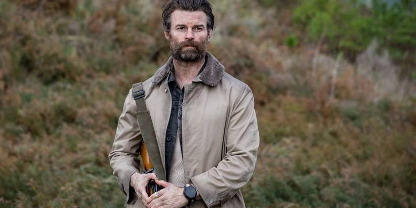 Daniel Gillies as Mandrake, standing in a field holding a gun in Coming Home in The Dark