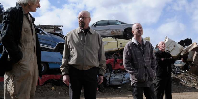 The cast stand in a junkyard with old cars piled on top of each other in Breaking Bad episode Live Free or Die.