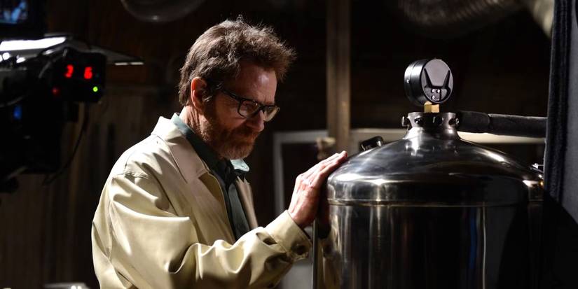 Walter White with shaggy hair and a beard, standing in a room with a hand on a tank in the Breaking Bad finale.