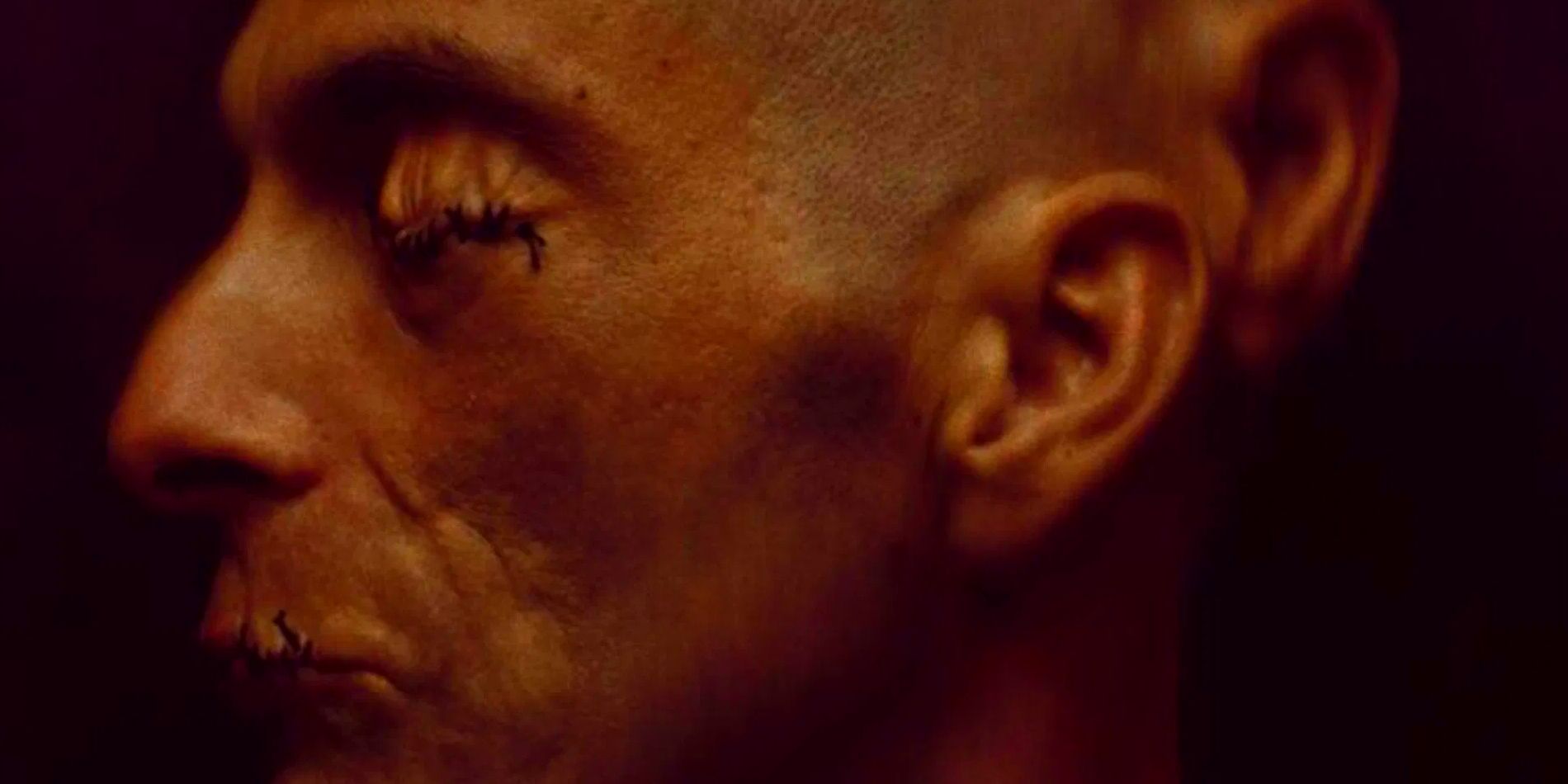 A side profile shot of a man with his eyes and mouth sewn shut and a second pair of ears in Crimes of the Future.
