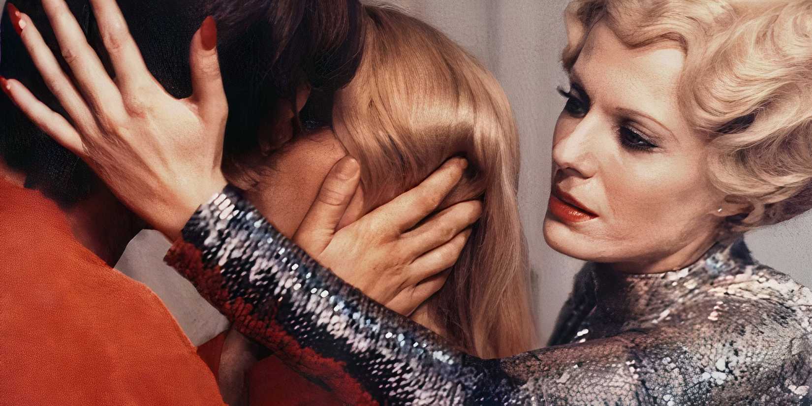 Delphine Seyrig in Daughters of Darkness holding a man's head while he kisses a woman.