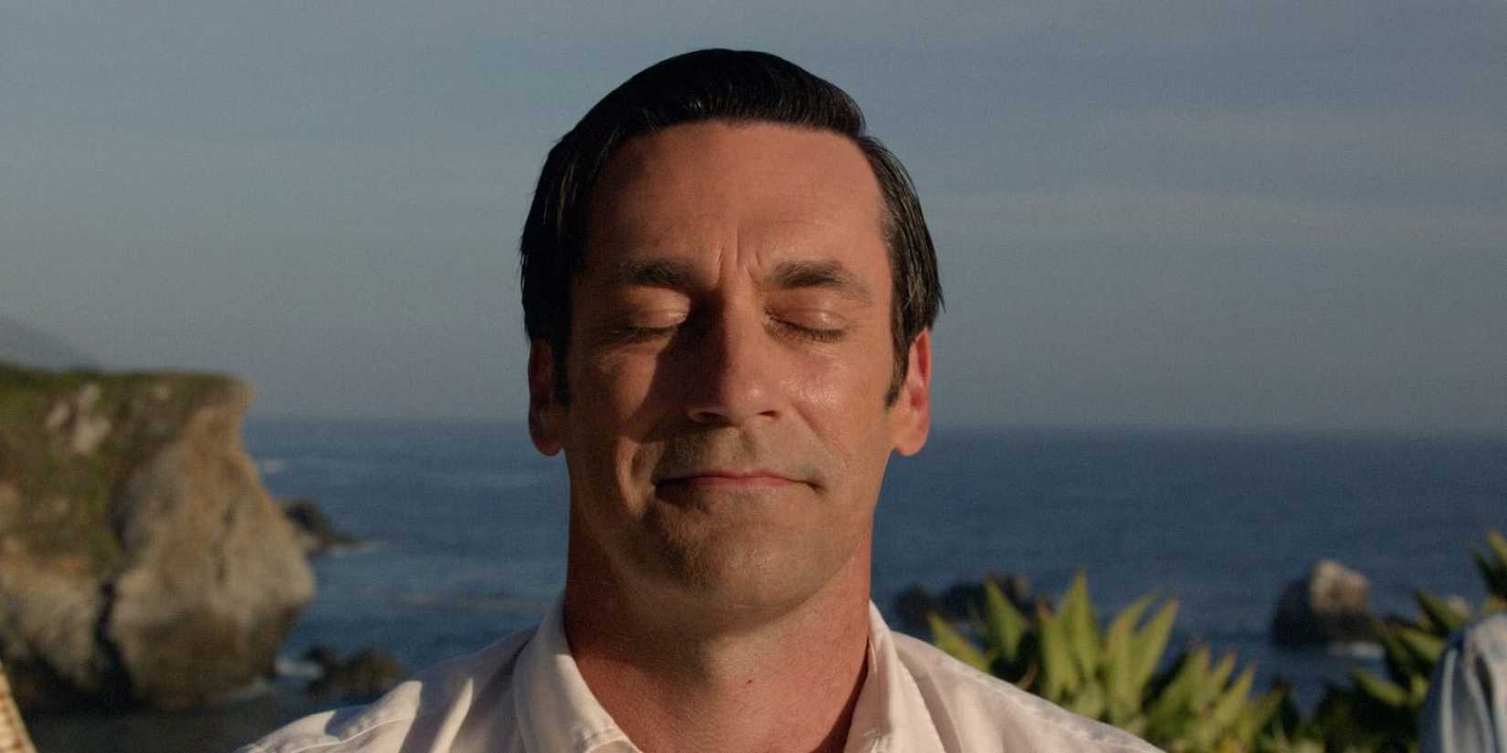 Don Draper sits on the grass by an ocean in a meditation pose with others behind him in the Mad Men finale.