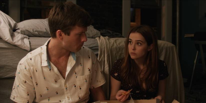 Glen Powell and Zoey Deutch eating pizza on a bedroom floor 'Set It Up'.