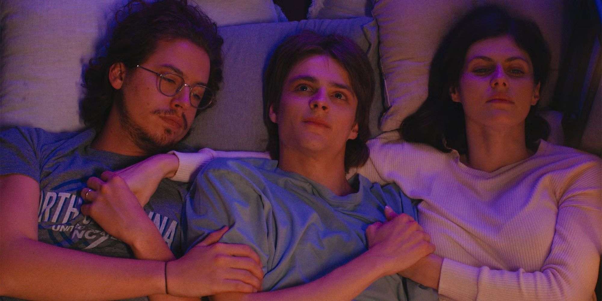 Cole Sprouse, Corey Fogelmanis, and Alexandra Daddario lie in bed holding hands in I Wish You All the Best.