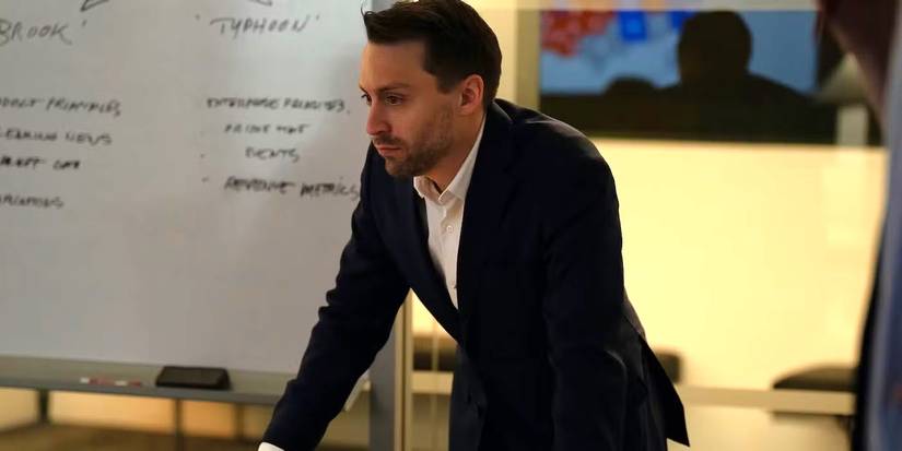 Kieran Culkin as Roman Roy leaning on a table in front of a white board in Succession Season 4, Episode 8.