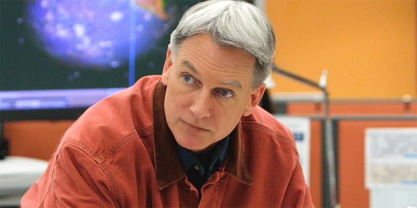 Mark Harmon as Gibbs looking over at someone while hunched over a desk in NCIS.