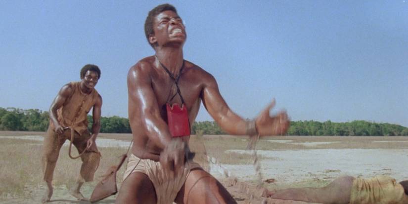 LeVar Burton as Kunta Kinte with shackles around his hands is whipped in Roots.