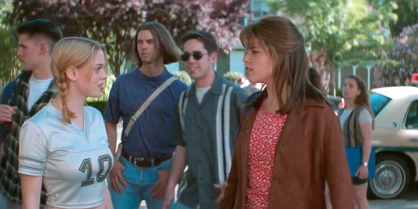 Tatum (Rose McGowan) stands next to Sidney (Neve Campbell) with other students walking behind them in Scream (1996).