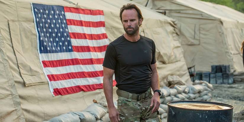 Walton Goggins sebagai Rip Taggart berdiri di luar tenda dengan bendera Amerika di sisinya di SIX.