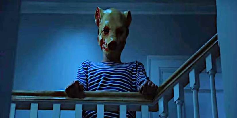 A young Cam wears a bloody pig mask and stands at the top of a stair railing in Slasher's The Executioner.