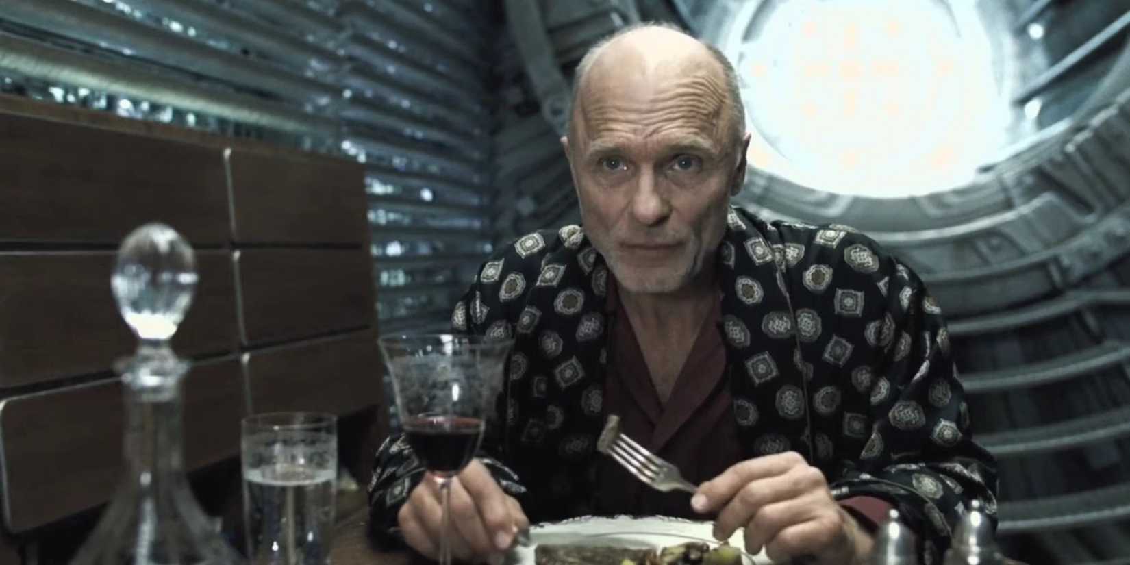 Ed Harris as Wilford eating dinner in Snowpiercer.