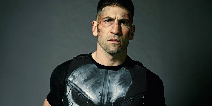 Jon Bernthal stares into the camera with a beaten face and a skull t-shirt for The Punisher.