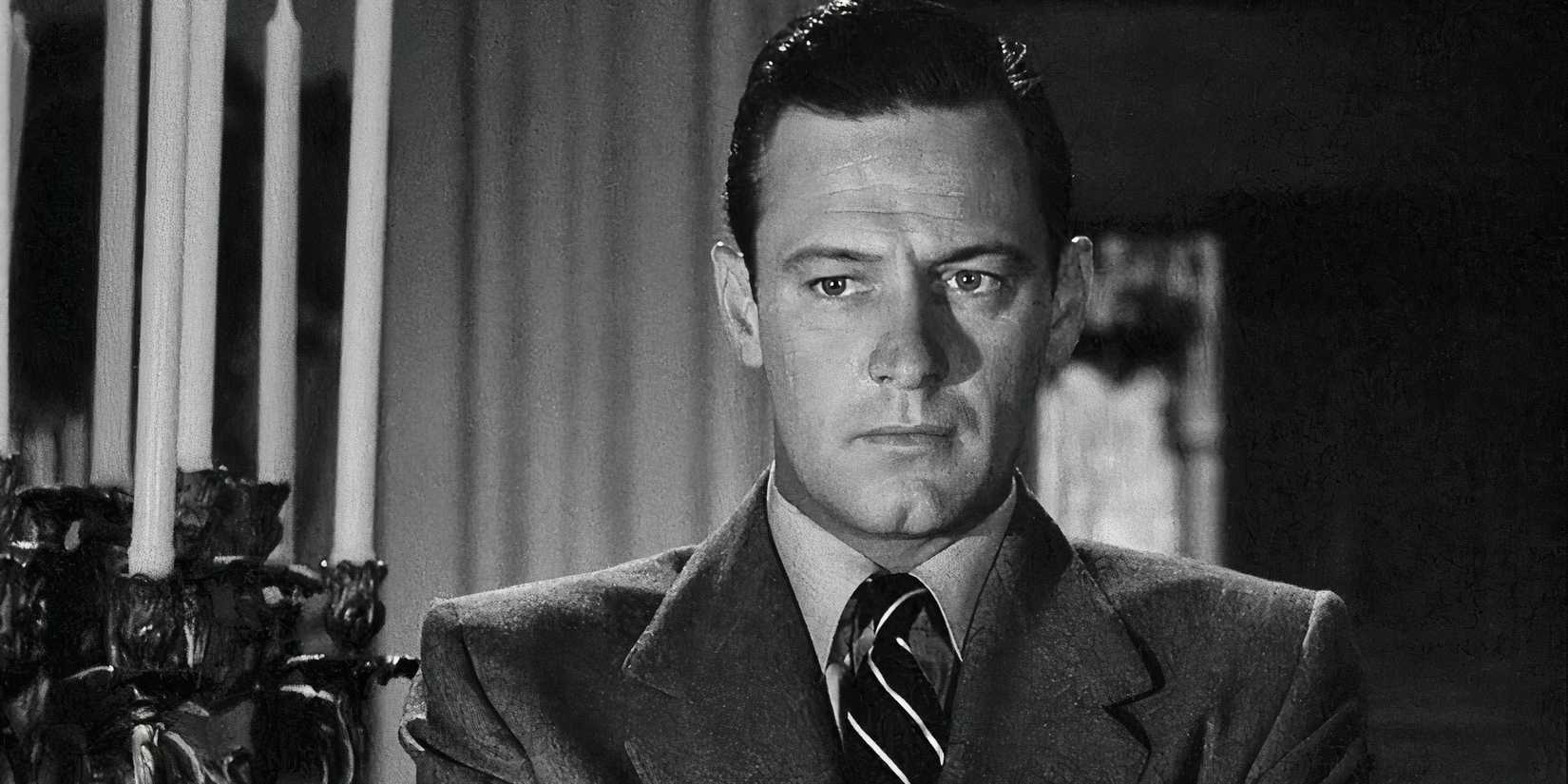 William Holden as Joe Gillis standing next to a candelabra and looking serious in Sunset Boulevard (1950).