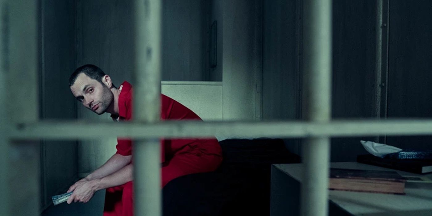 Penn Badgley as Joe Golberg wearing a red jumpsuit and looking through the bars of a prison cell in You Season 5