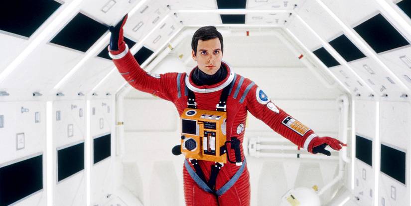 Keir Dullea in a red spacesuit walking through well-lit space pod in 2001: A Space Odyssey.