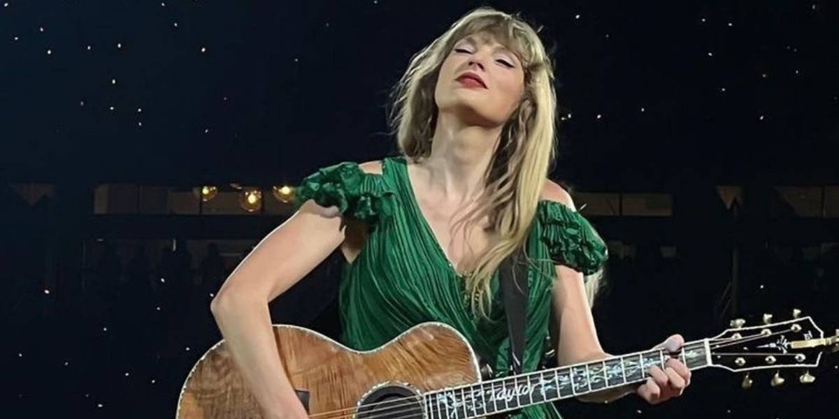 Taylor Swift em um vestido verde tocando violão na Eras Tour.