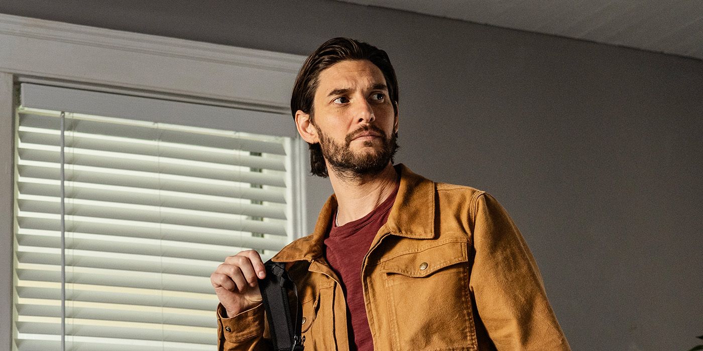 Ben Barnes sebagai Tim berdiri di dalam rumah di samping jendela dengan tirai di The Institute
